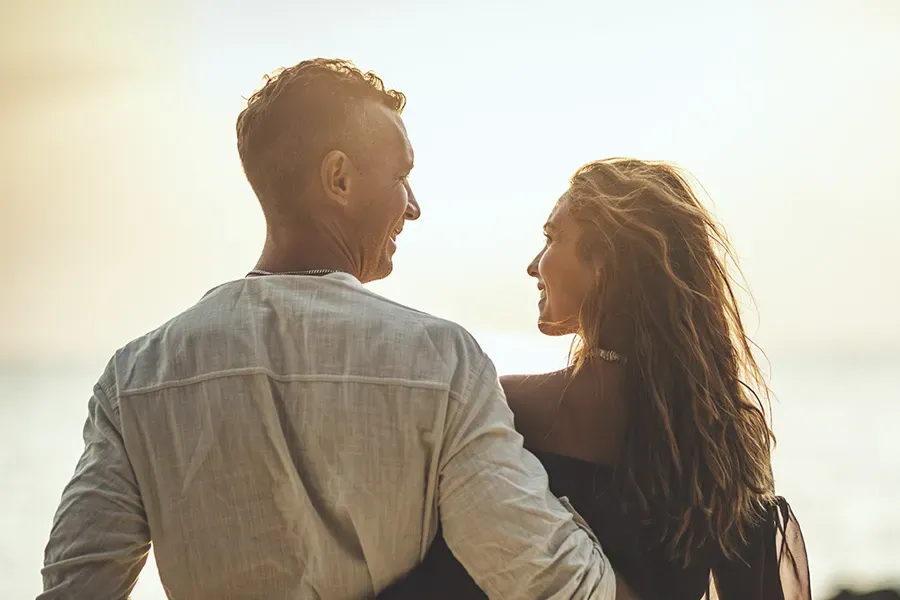 A couple gazes at each other on the beach at sunrise, viewed from behind. Schedule Anti-Aging treatment from Don D. Fisher, D.O. at The BEST Program in Fort Lauderdale.