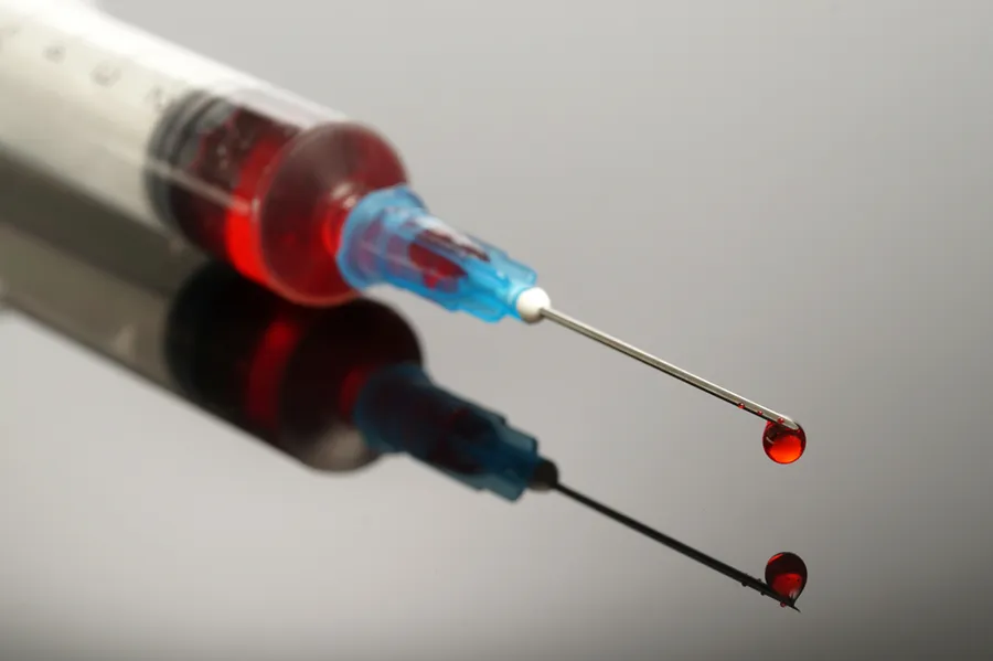A close-up of a medical syringe filled with a red liquid, capturing a drop of the liquid falling from the needle. Lipo-B12 Weight Loss Injecitons offered by Don D. Fisher, D.O. at The BEST Program in Fort Lauderdale.