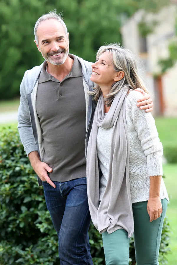 A mature couple in gray toned clothes and jeans walk happily outside, happy with their successful bioidentical hormone treatments from Don D. Fisher, D.O. at The BEST Program in Fort Lauderdale.