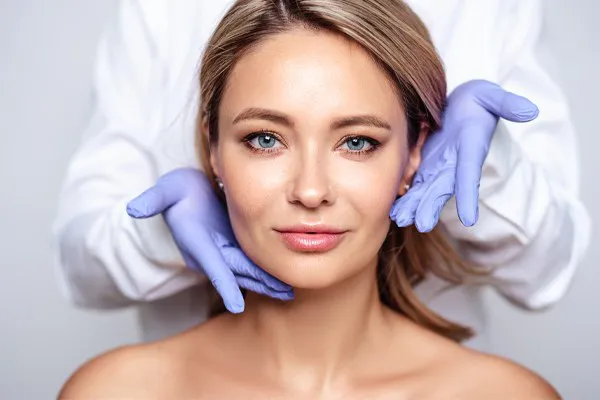 Close up of a woman's face with a doctor wearing rubber gloves standing behind her holding his hands around her face to show the amazing Botox Cosmetic treatment from Don D. Fisher, D.O. at The BEST Program in Fort Lauderdale.