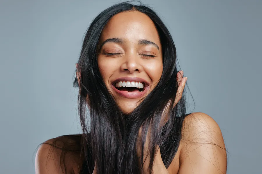 A woman runs her fingers through her long, thick, lustrous hair. Get exosomes for hair restoration from Don D. Fisher, D.O. at The BEST Program in Fort Lauderdale.
