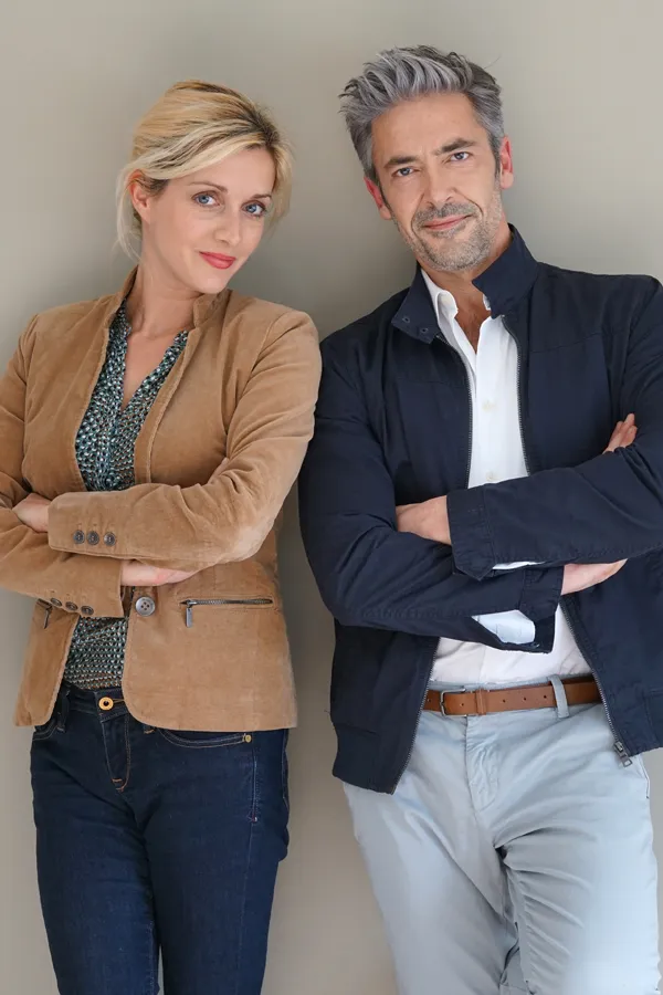 A middle-aged couple stand against a wall smiling with folded arms. Get hyperthyroidism treatment from Don D. Fisher, D.O. at The BEST Program in Fort Lauderdale.