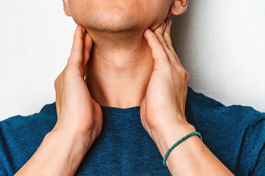 A man in a dark teal shirt rubs the lymph nodes on his neck. Get hypothyroidism treatment from Don D. Fisher, D.O. at The BEST Program in Fort Lauderdale.