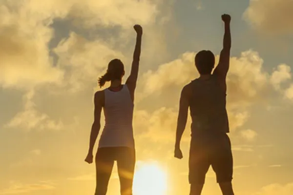 A couple raise their right arms in the air in triumph, framed by the sunrise. Get Ipamorelin peptide treatment from Don D. Fisher, D.O. at The BEST Program in Fort Lauderdale.
