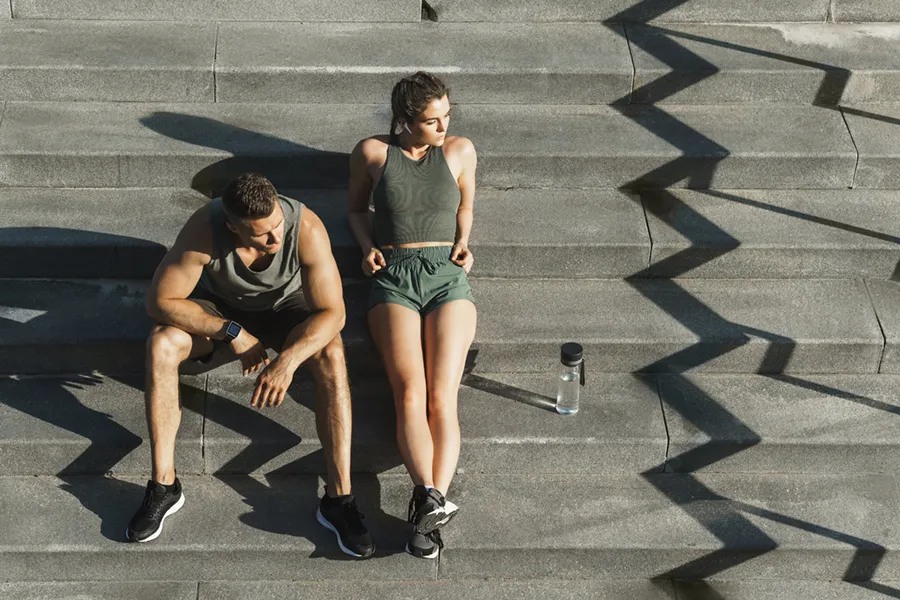 A couple in gray and green track clothes resting after a workout on stone steps, happy with their weight loss plans from Don D. Fisher, D.O. at The BEST Program in Fort Lauderdale.