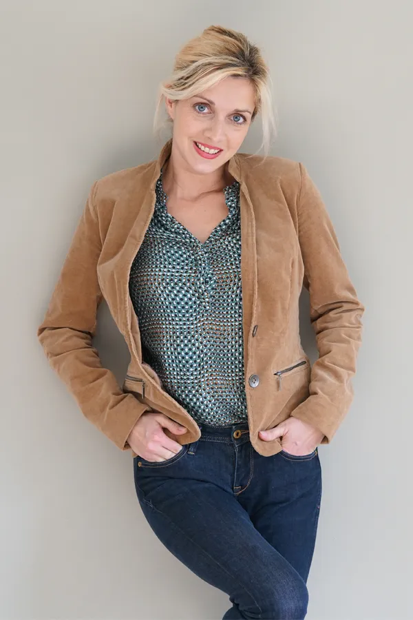 A smiling blonde woman in a tan leather jacket leans against a gray wall. Schedule metabolic syndrome from Don D. Fisher, D.O. at The BEST Program in Fort Lauderdale.