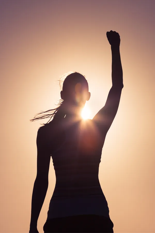 A woman raises her fist in the air, silhouetted by the sun. Get methylene blue IV therapy from Don D. Fisher, D.O. at The BEST Program in Fort Lauderdale.