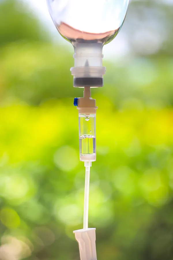 Close-up of an IV drip against a forest background. Get the Myers Cocktail IV treatment from Don D. Fisher, D.O. at The BEST Program in Fort Lauderdale.