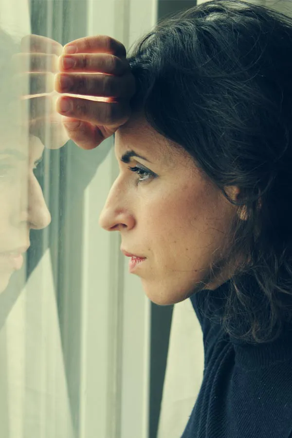 A brunette woman in a thin dark turtleneck looks out the window with a serious expression, suffering from PCOS. Get treatment for Polycistic Ovarian Syndrome/PCOS from Don D. Fisher, D.O. at The BEST Program in Fort Lauderdale.