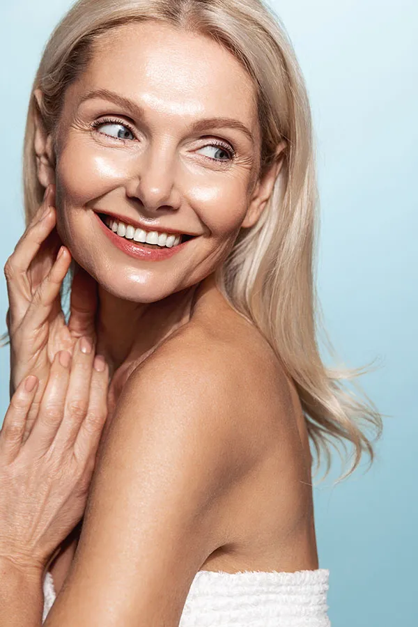 An older blonde woman touches her face to feel the beautiful results of her PDO thread lift treatment from Don D. Fisher, D.O. at The BEST Program in Fort Lauderdale.