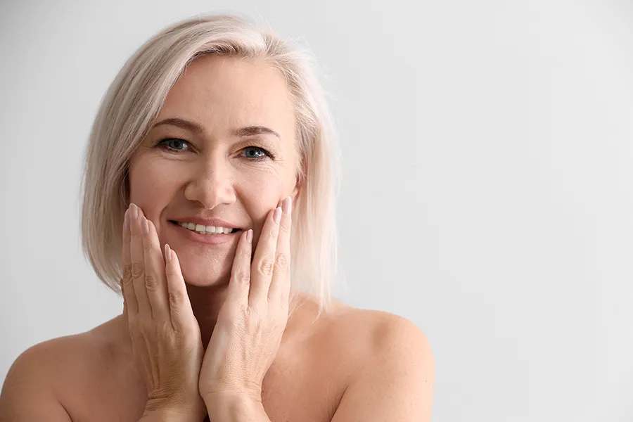 PRP-Microneedling-Clinic A mature woman touches her faces to feel the successful results of PRP microneedling and skin rejuvenation treatments from Don D. Fisher, D.O. at The BEST Program in Fort Lauderdale.