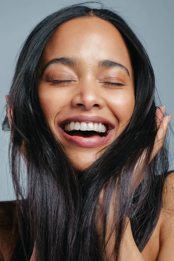 A beautiful latin woman smiles and runs her fingers through her long, beautiful hair, happy with her PRP for hair loss and restoration treatment from Don D. Fisher, D.O. at The BEST Program in Fort Lauderdale.