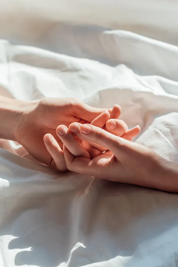 A close up of a man and woman's hands lightly clasping on a bedsheet, representing successful PT141 sexual wellness treatment for women from Don D. Fisher, D.O. at The BEST Program in Fort Lauderdale.
