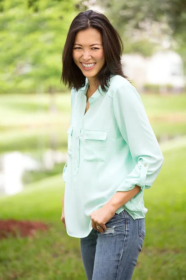 A middle-aged brunette woman in a light green button-up shirt stands outside smiling, happy with her perimenopause treatment from Don D. Fisher, D.O. at The BEST Program in Fort Lauderdale.