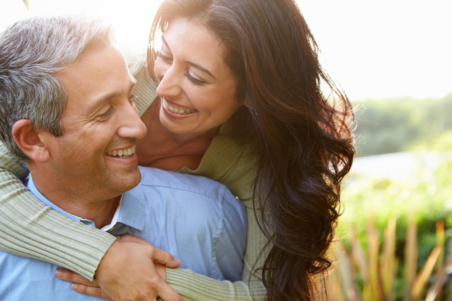 A middle-aged latin couple embrace playfully in a green field. Get regenerative exosome IV therapy from Don D. Fisher, D.O. at The BEST Program in Fort Lauderdale.