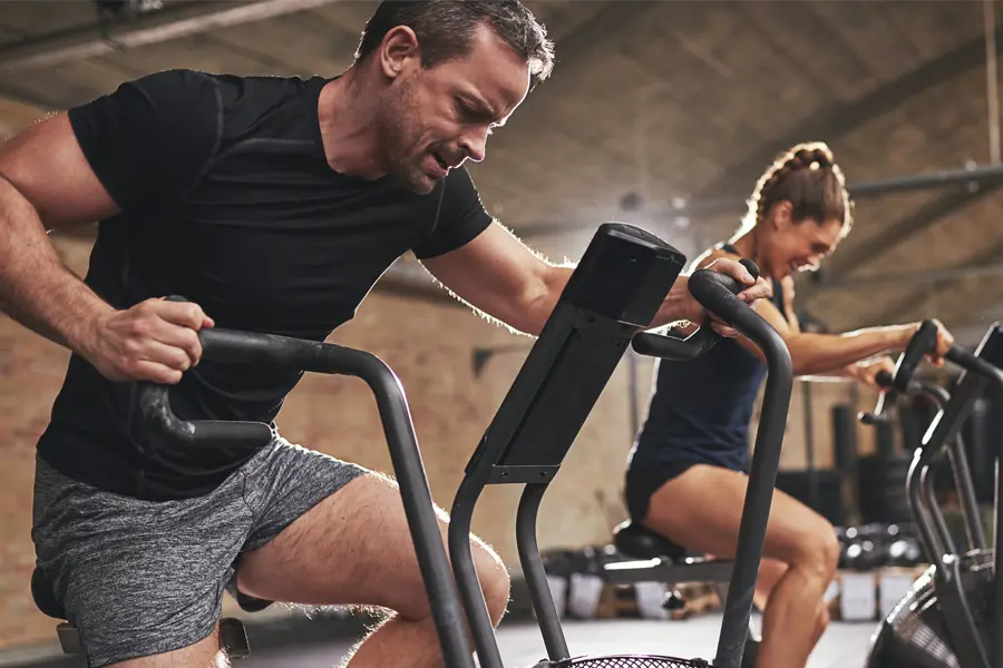 A couple in a brick gym work as hard as they can on exercise bikes, inspired by successful Tirzepatide treatment from Don D. Fisher, D.O. at The BEST Program in Fort Lauderdale.