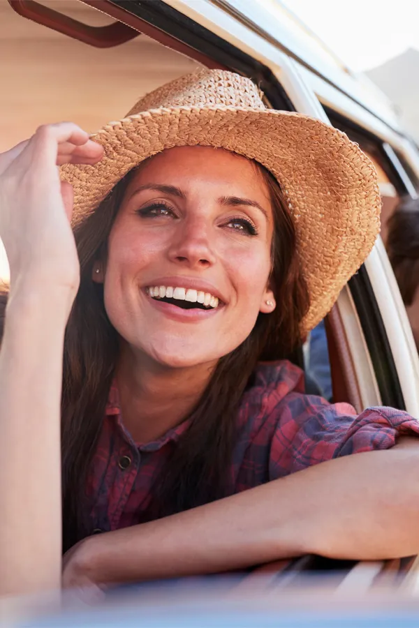 A woman with a sun hat leans out a car window smiling. Get Rapid-D Vitamin injections from Don D. Fisher, D.O. at The BEST Program in Fort Lauderdale.