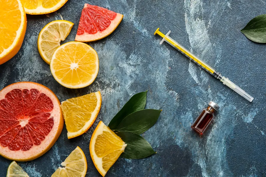 A gray marble countertop covered with sliced fruit and a syringe and vial, representing vitamin injections from Don D. Fisher, D.O. at The BEST Program in Fort Lauderdale.
