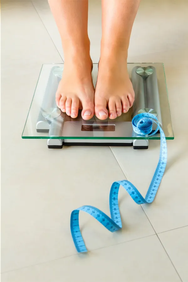 Close-up of a woman's feet standing on a scale, with measuring tape by her toes, getting treatment for weight loss resistance from Don D. Fisher, D.O. at The BEST Program in Fort Lauderdale.